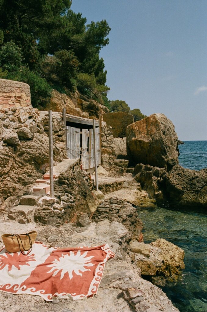 Towels and a beach bag on the rocks beside a clear-water cove in Ibiza.