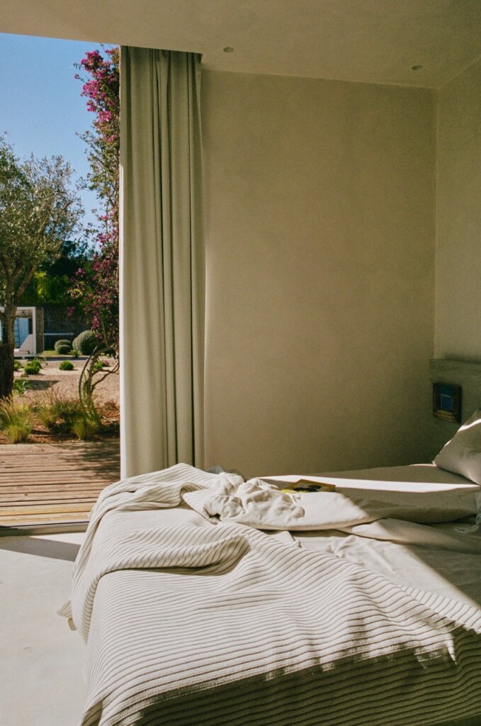 White linen bed beside open garden doors in a serene bedroom at luxury villa Can Paloma, Ibiza.