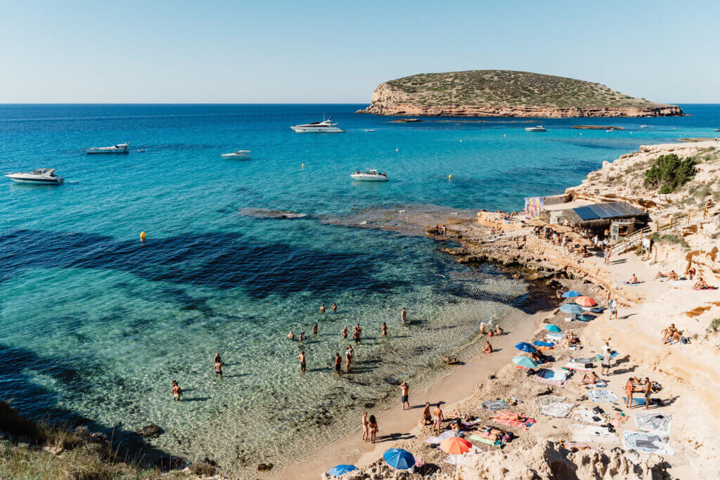 The turquoise waters of Cala Comte beach in Ibiza, located near luxury Villa Anaïs, featuring white yachts and a sandy shoreline.