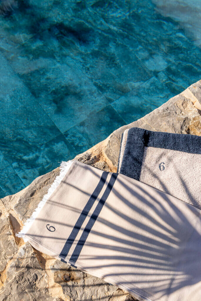 Embroidered beige towels resting on the stone edge of the luxury Villa Anaïs swimming pool with palm leaf shadows.