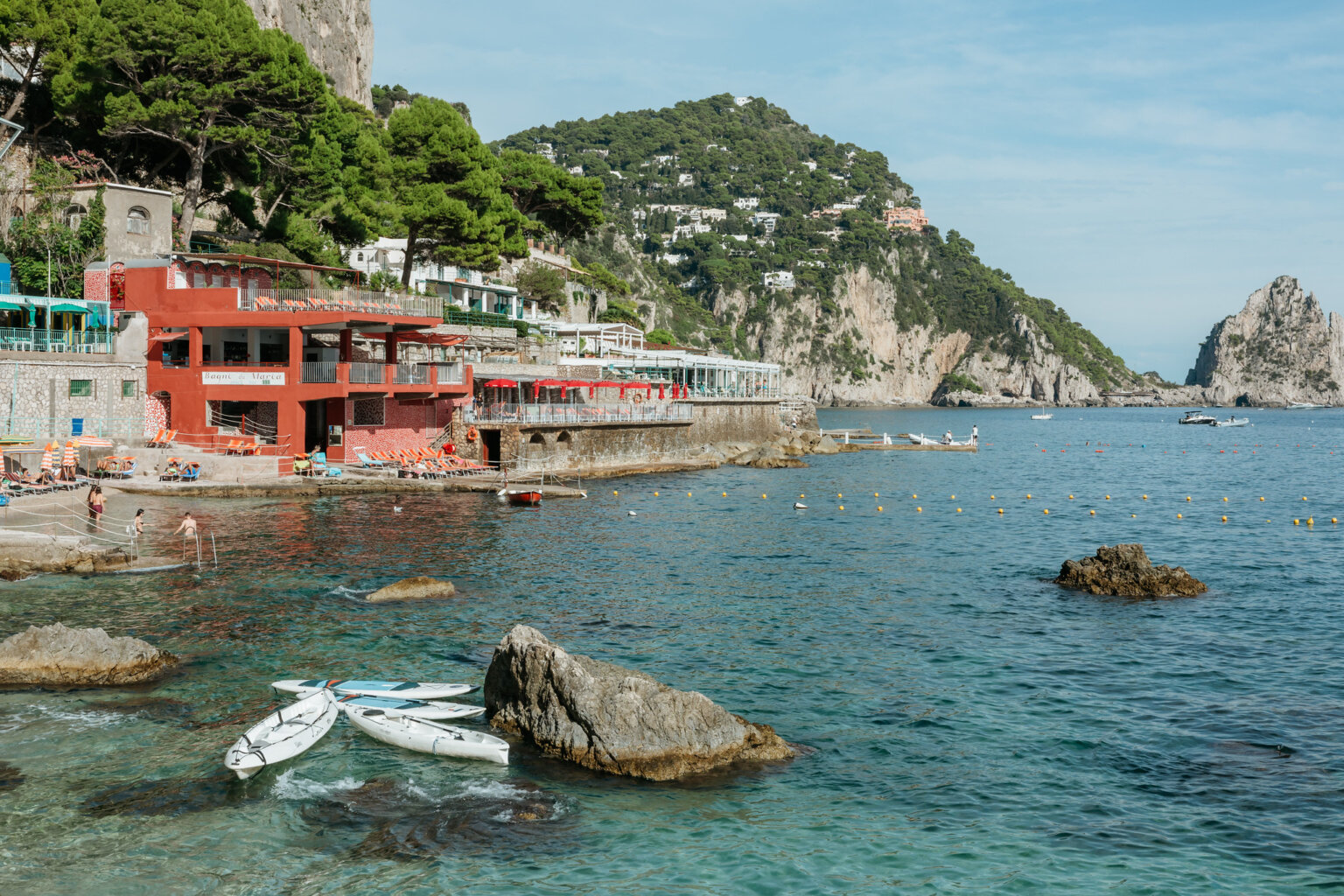 Seaside beach club on Capri with rocky shoreline and views toward the Faraglioni