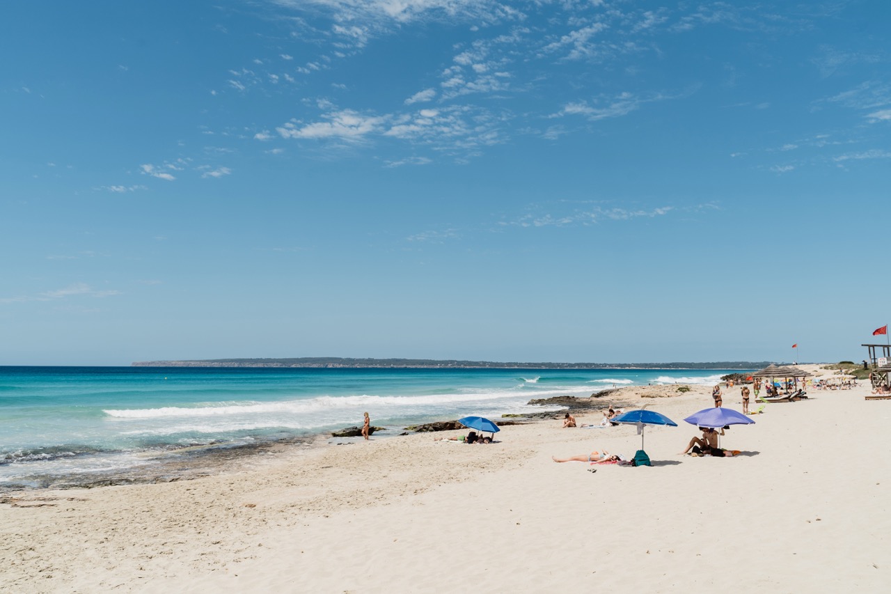 Sunbathers and blue umbrellas on the sandy shore at Arenals beach, Formentera.