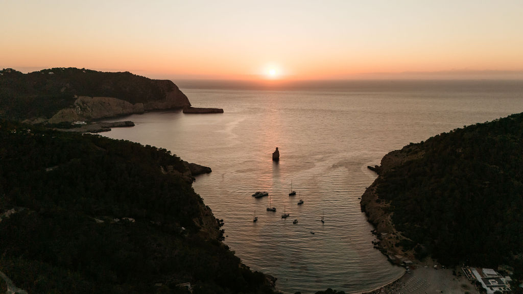 Sun setting over the sea at Benirràs cove, Ibiza, with boats anchored offshore.