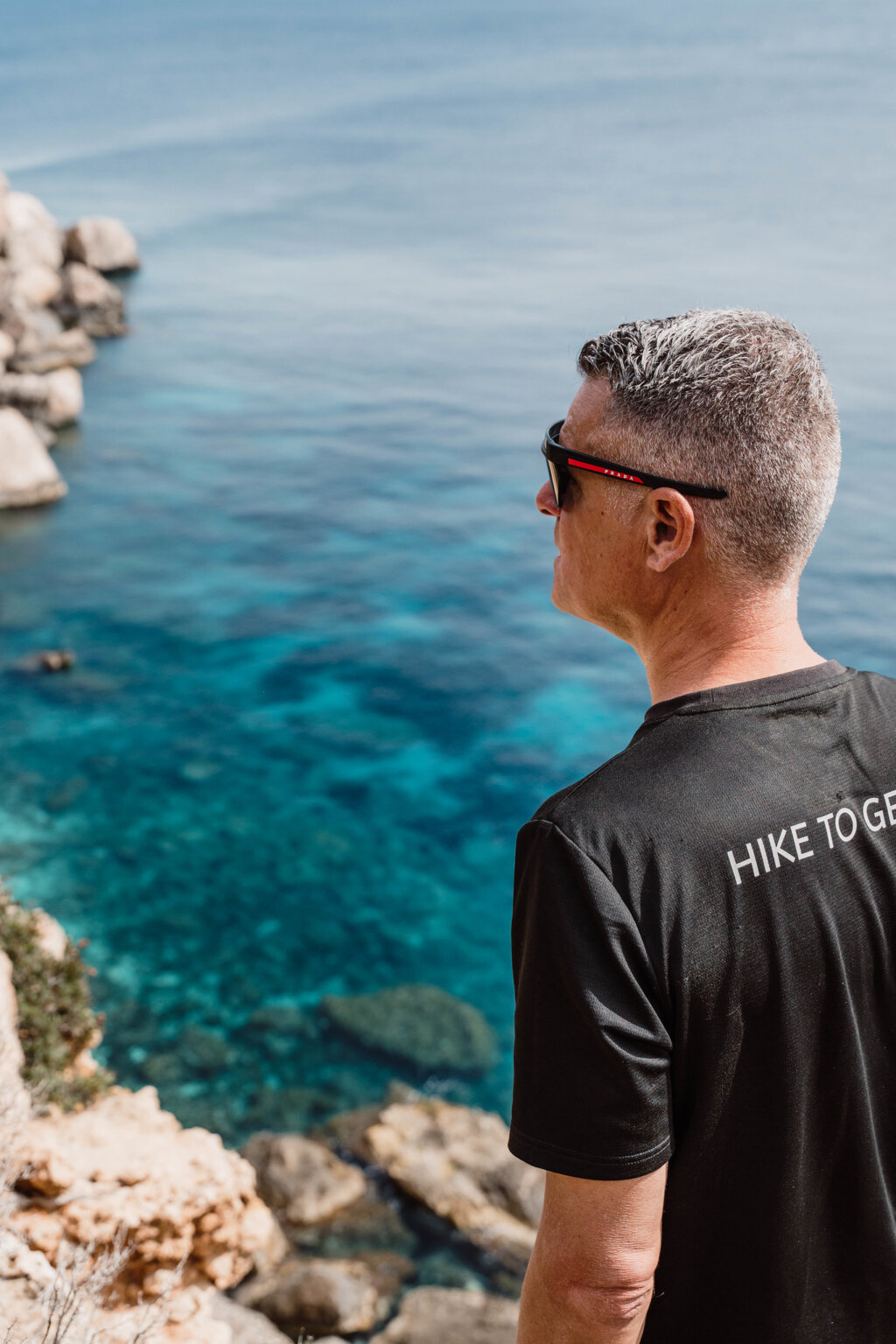 Hiker looking out over clear turquoise water from Ibiza's rocky coastline.