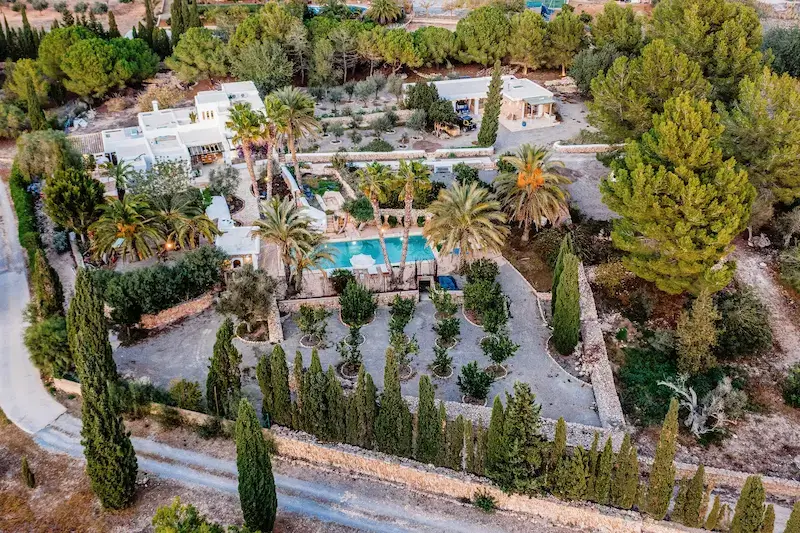 Aerial view of Can Sabina Villa, Ibiza, showing the pool, surrounding gardens, and tree-lined grounds.