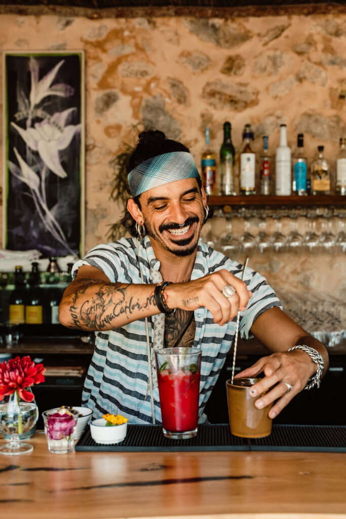 Bartender preparing drinks at La Paloma in Ibiza, with a stone bar and bottles behind him.
