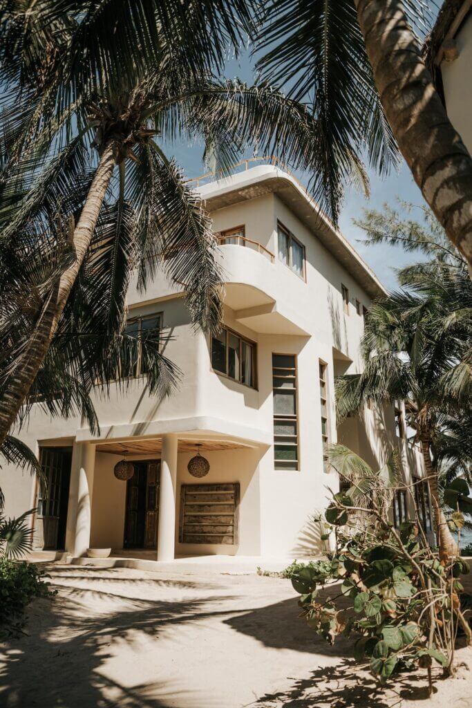 White villa framed by palm trees, with a shaded entrance and upper balcony.