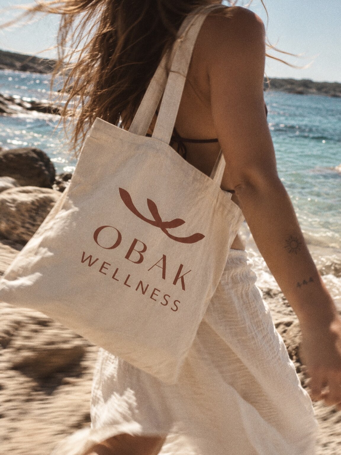 OBAK Wellness canvas tote carried beside the sea on Formentera's rocky shore.