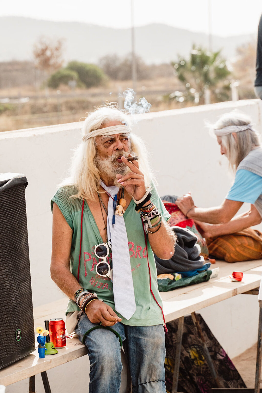 Marketgoer with long white hair seated beside a table at Sant Jordi Flea Market, Ibiza.