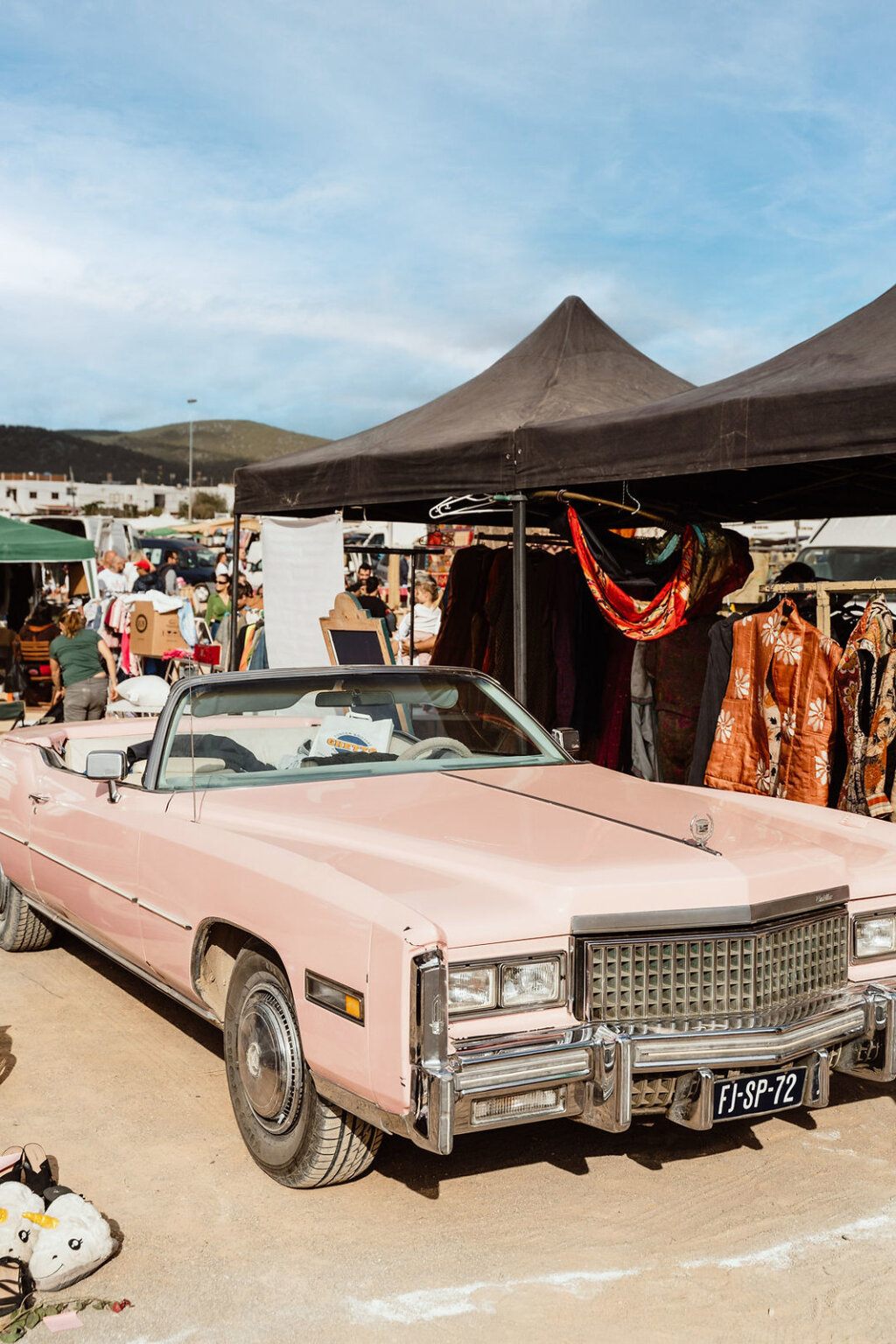 Vintage pink convertible parked beside clothing stalls at Sant Jordi Flea Market, Ibiza.